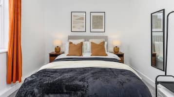 Een hotelkamer met een bed, twee nachtkastjes, een spiegel en een raam met gordijnen.
