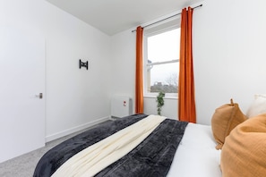 Quarto de hotel com cama, radiador, janela com cortinas e porta.