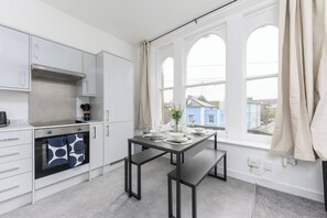 Uma cozinha moderna com armários brancos, forno embutido e um espaço de jantar com mesa posta para dois.