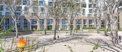 Un edificio moderno con varios pisos, balcones y un patio con árboles y senderos de grava.