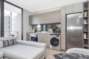 Um apartamento moderno com cozinha compacta, máquina de lavar, frigorífico e sofá.