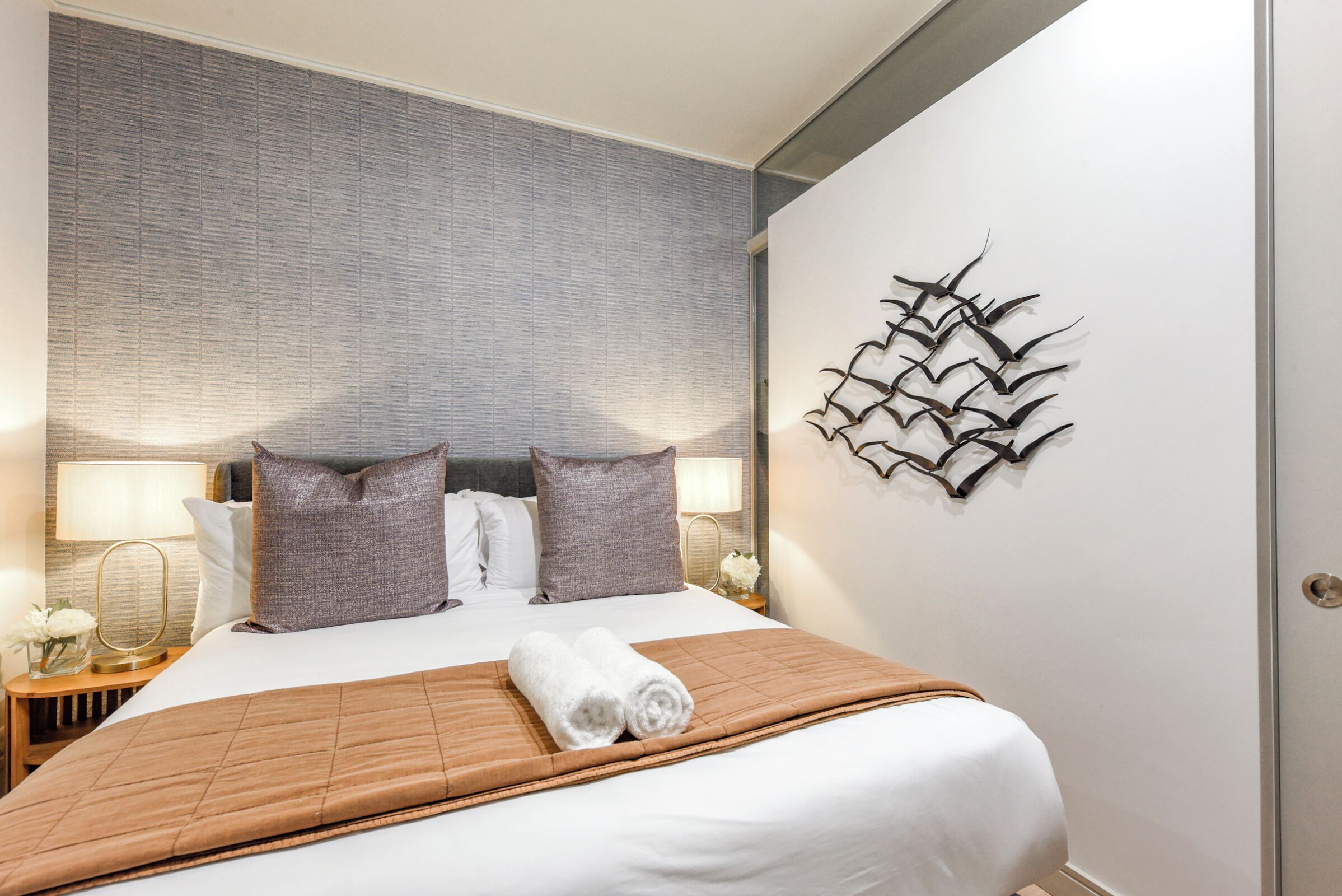 Ein Hotelzimmer mit einem großen Bett, zwei Kissen, einem Wandbild und einem Nachttisch mit Lampe und Blumen.