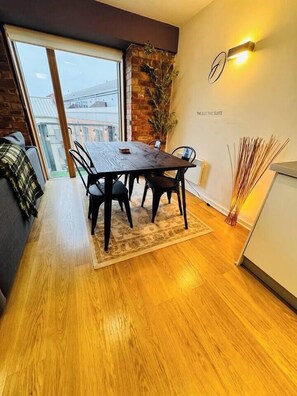 A dining area with a wooden table and chairs, a small rug, a plant, and a wall-mounted light fixture. - #12 CozyCanalsideLoft|near CoventryCathedral|for 6 (West Midlands)