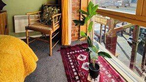 Ein Zimmer mit großem Fenster, einem Sessel, einer Pflanze und einem gemusterten Teppich.