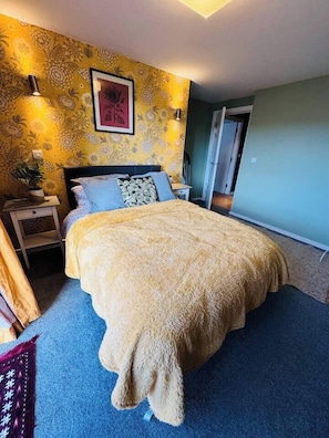 Ein Schlafzimmer mit einem Bett, einem Nachttisch, einer Lampe und einer Wand mit floralem Muster.