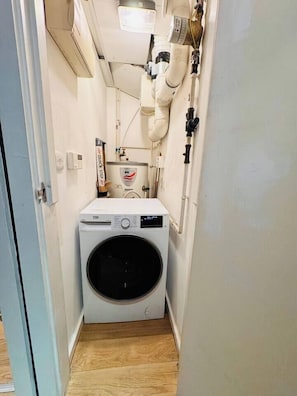 A compact laundry room with a front-loading washing machine, a water heater, and a vent system. - #12 CozyCanalsideLoft|near CoventryCathedral|for 6 (West Midlands)