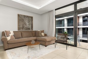 Un salon moderne avec un canapé d’angle, une table basse et une grande fenêtre donnant sur l’extérieur.