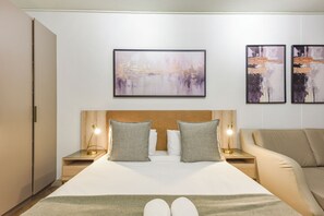 Une chambre d’hôtel comprenant un lit, deux lampes de chevet, une tête de lit, un canapé et trois œuvres d’art encadrées accrochées au mur.