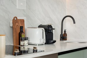 Una cocina con encimera blanca, cafetera, tostadora y una botella de aceite de oliva.