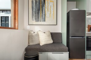 Eine Küchenzeile mit einem schwarzen Kühlschrank, einem grauen Sofa mit gemusterten Kissen und einem kleinen Hocker.