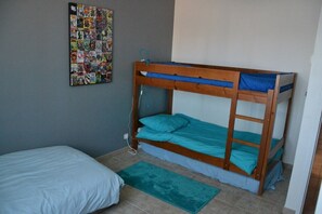 Ein Etagenbett mit blauer Matratze, ein Einzelbett mit weißer Matratze und ein an der Wand befestigtes Comic-Poster.