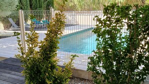 A swimming pool surrounded by a fence, with a pebble bed in the foreground and greenery in the background. - House Sleeps 14 + Pool + Air Conditioning + Outdoor Kitchen (Adissan)