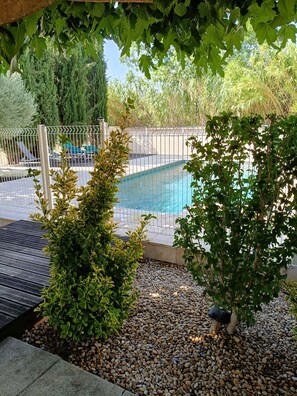 Ein Pool, umgeben von einem Zaun, mit Kiesbett im Vordergrund und Grünflächen im Hintergrund.