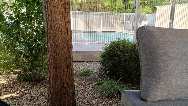 A wooden deck with a bench, a tree, and a view of a swimming pool. - House Sleeps 14 + Pool + Air Conditioning + Outdoor Kitchen (Adissan)