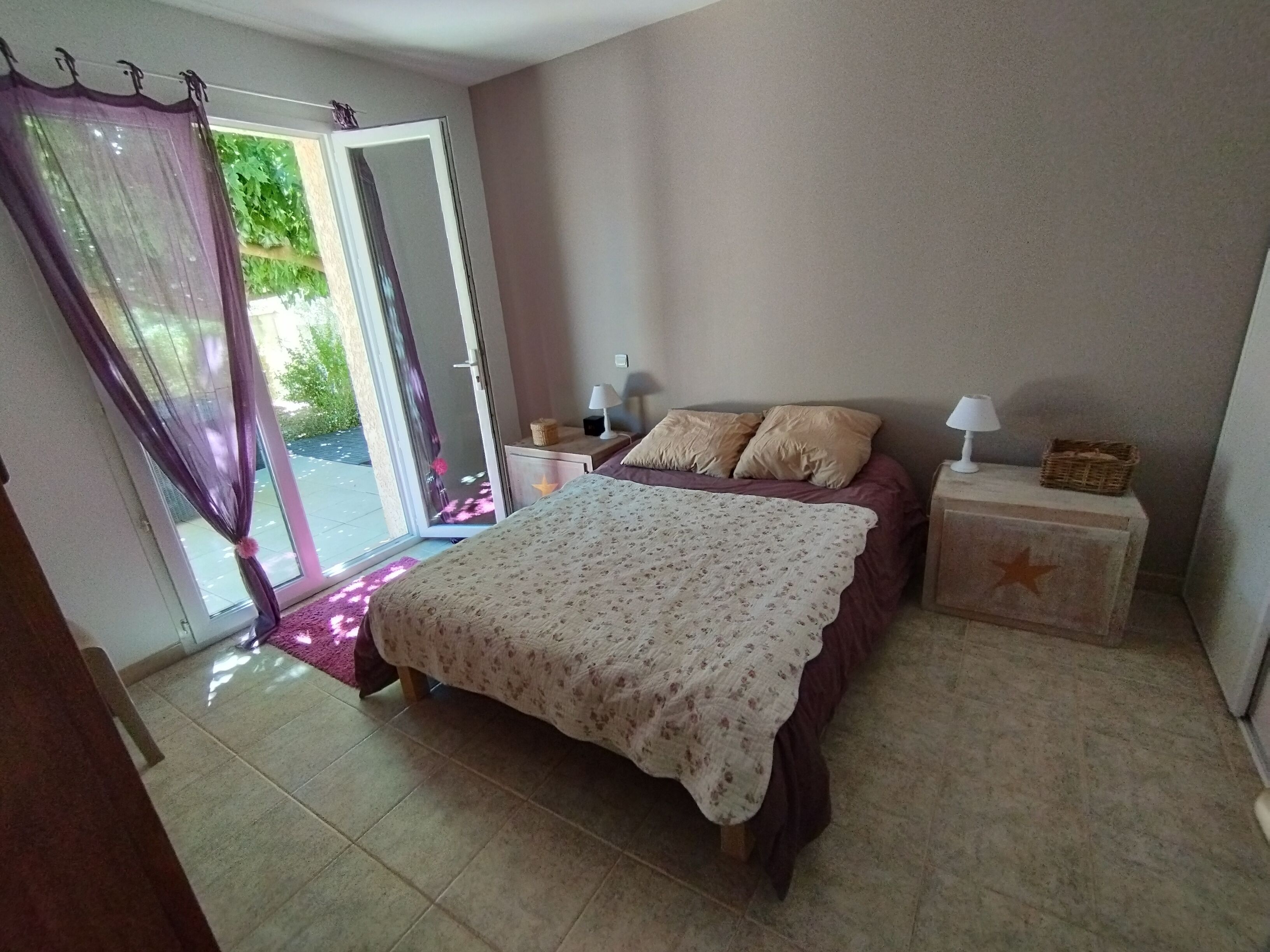 A bedroom with a bed, a nightstand, a lamp, and a window with curtains.
