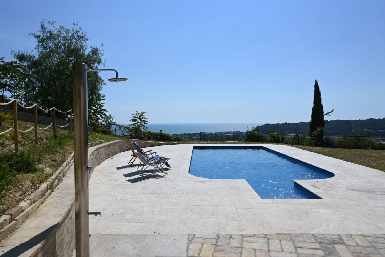 Piscina con vistas claras al mar, rodeada por una terraza de piedra y algunas sillas de descanso.