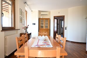 Una zona de menjador amb una taula de fusta, cadires, un camell de taula amb motius florals i un armari amb portes de vidre.