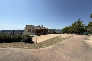 A single-story stone building with a flat roof, a paved patio, and a view of the countryside.