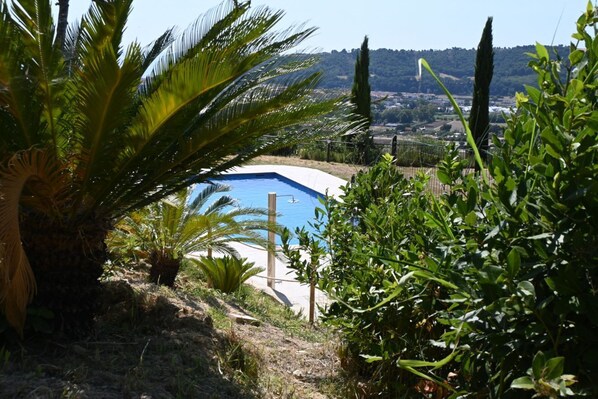 A swimming pool surrounded by lush greenery and a view of a distant town.