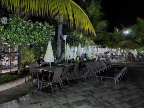 Een terras met tafels, stoelen, parasols en palmbomen.