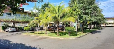 A residential street with parked cars, palm trees, and houses.