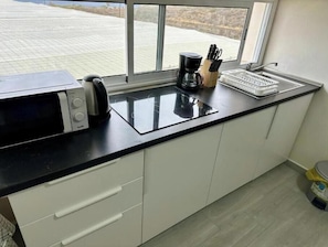 Eine Küche mit Mikrowelle, Kaffeemaschine und Geschirr auf der Arbeitsplatte, mit Blick aus dem Fenster auf ein schachbrettartiges Stadtbild.