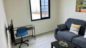 Un salon comprenant un canapé, une table basse, un bureau avec une chaise, une fenêtre donnant sur un paysage agréable et un tableau accroché au mur.