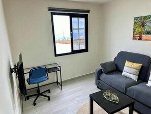 Ein Wohnzimmer mit einer Couch, einem Couchtisch, einem Schreibtisch mit Stuhl, einem Fenster mit Blick und einem Bild an der Wand.