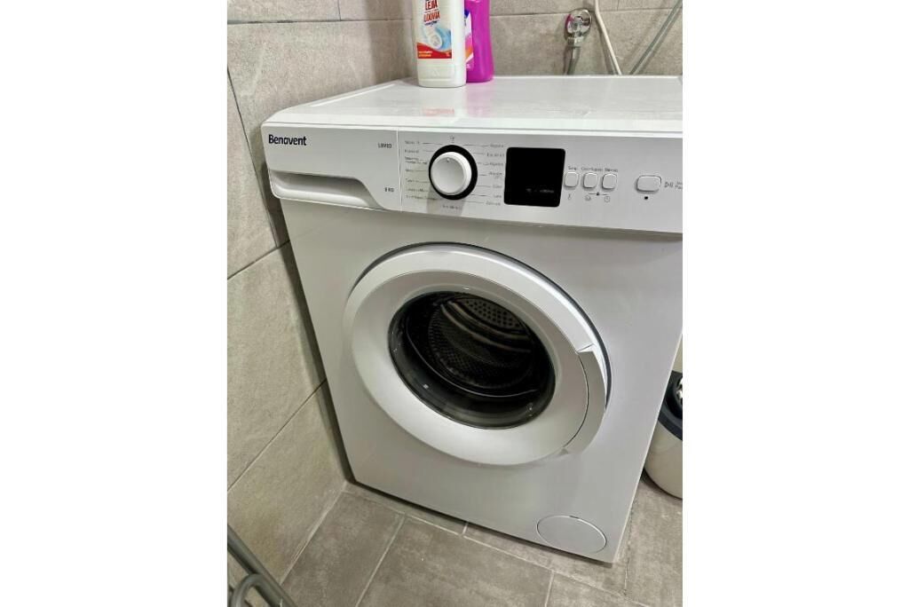 A Benavent washing machine in a bathroom with tiled walls and floor.