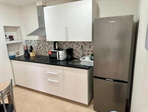 Eine Küche mit weißen Schränken, einem Edelstahlkühlschrank, einer schwarzen Arbeitsplatte und einer gefliesten Spritzschutzwand.