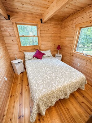Een slaapkamer met houten lambrisering, een bed, twee nachtkastjes en twee ramen.