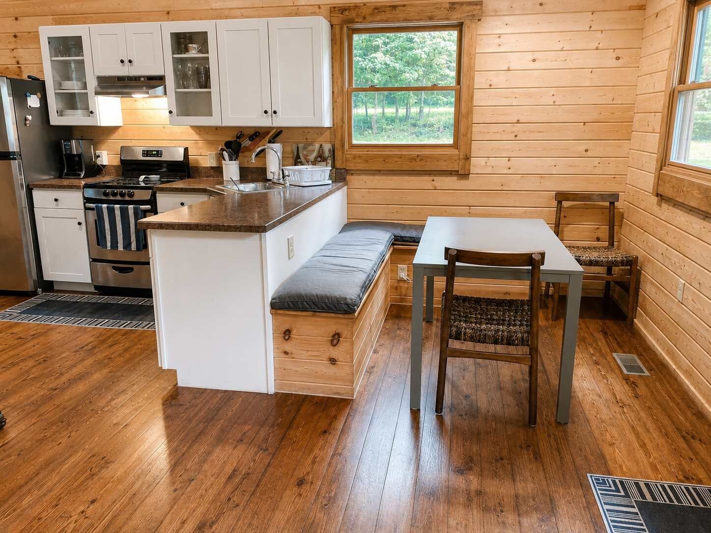 A compact kitchen with wooden cabinets, a stove, and a dining area with a bench and table.