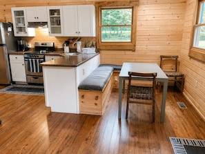 A compact kitchen with wooden cabinets, a stove, and a dining area with a bench and table.
