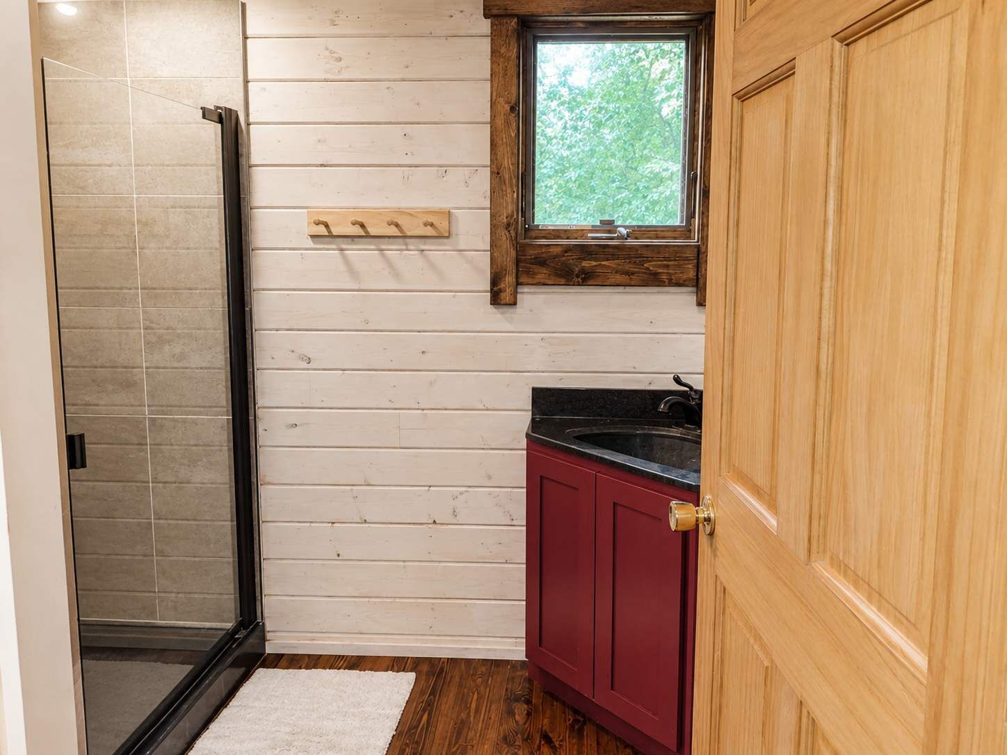A bathroom with a glass shower door, a wooden vanity with a sink, and a window above the mirror.