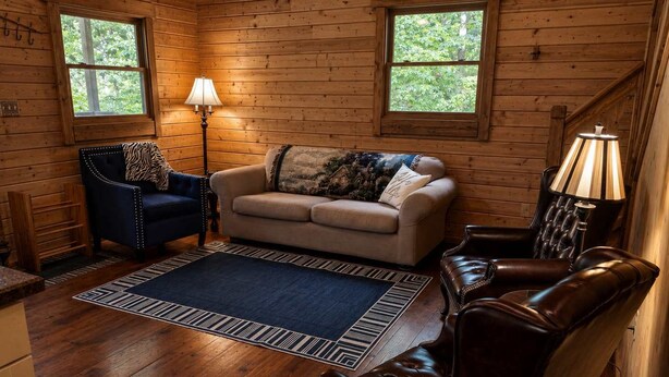 A cozy cabin interior with a sofa, armchair, and a lamp. - River Cabin w/Kayaks, Fire Pit, WiFi & Game Room (Great Cacapon)