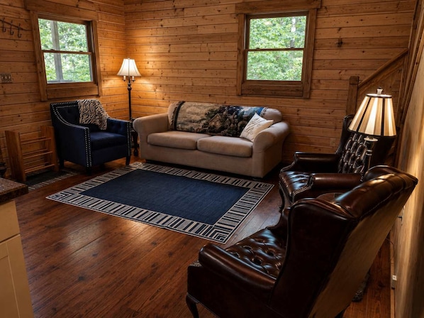 A cozy cabin interior with a sofa, armchair, and a lamp.