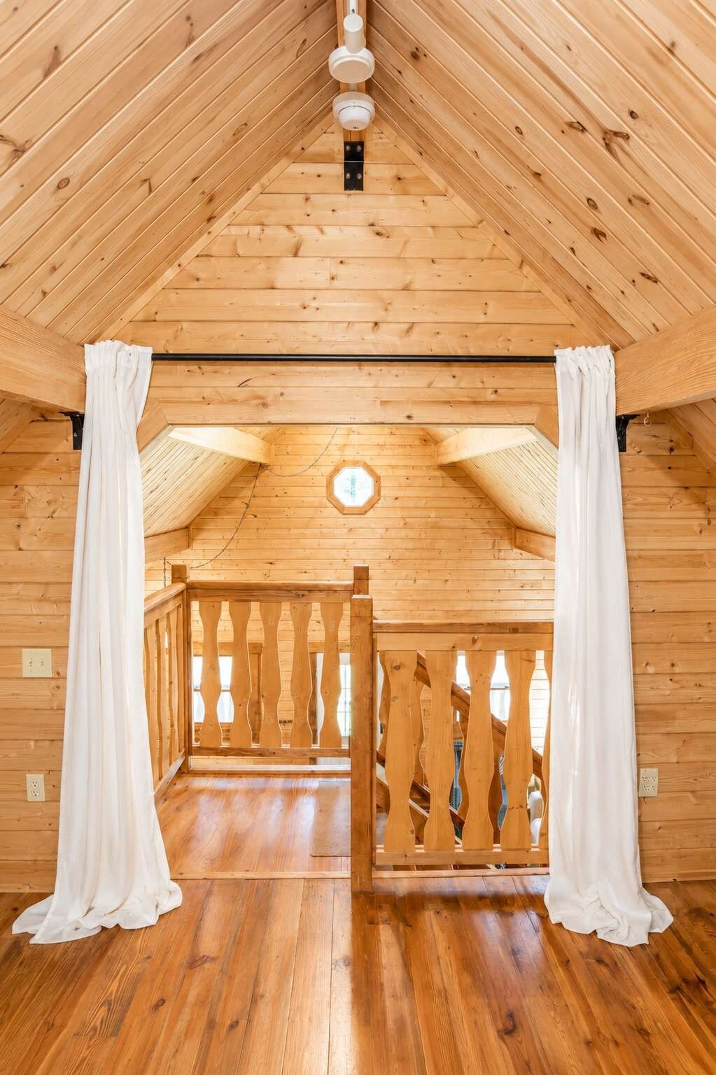 A wooden interior with a high ceiling, a wooden railing, and a view through the railing.