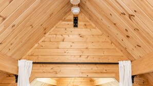 A wooden interior with a high ceiling, a wooden railing, and a view through the railing. - River Cabin w/Kayaks, Fire Pit, WiFi & Game Room (Great Cacapon)