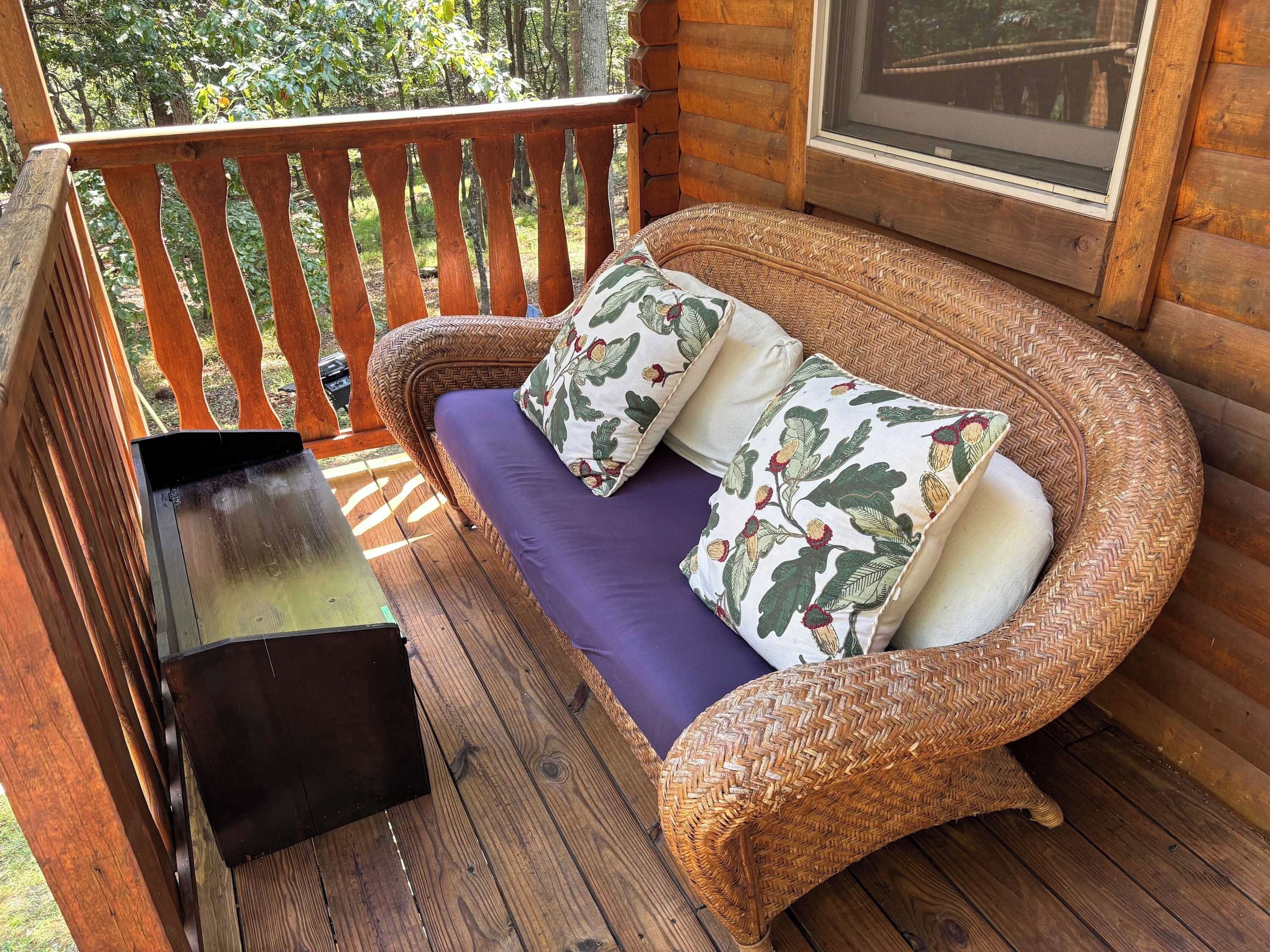 A wicker sofa with cushions on a wooden deck.