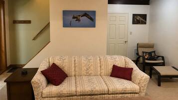 A living room with a sofa, a chair, a small table, a staircase, and a door.