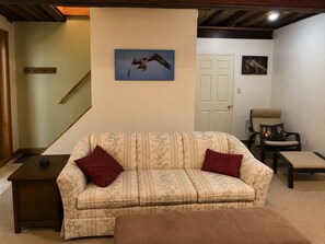 A living room with a sofa, a chair, a small table, a staircase, and a door.