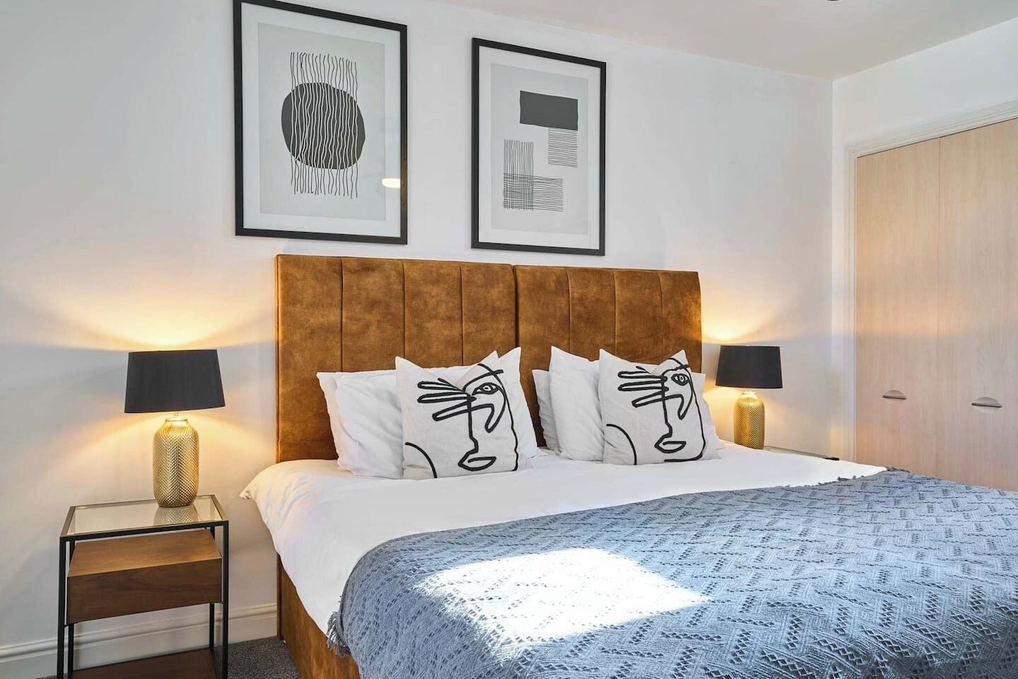A bedroom with a large bed, two bedside tables, a wooden wardrobe, and two framed artworks on the wall.