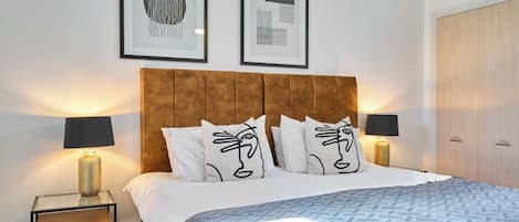A bedroom with a large bed, two bedside tables, a wooden wardrobe, and two framed artworks on the wall.