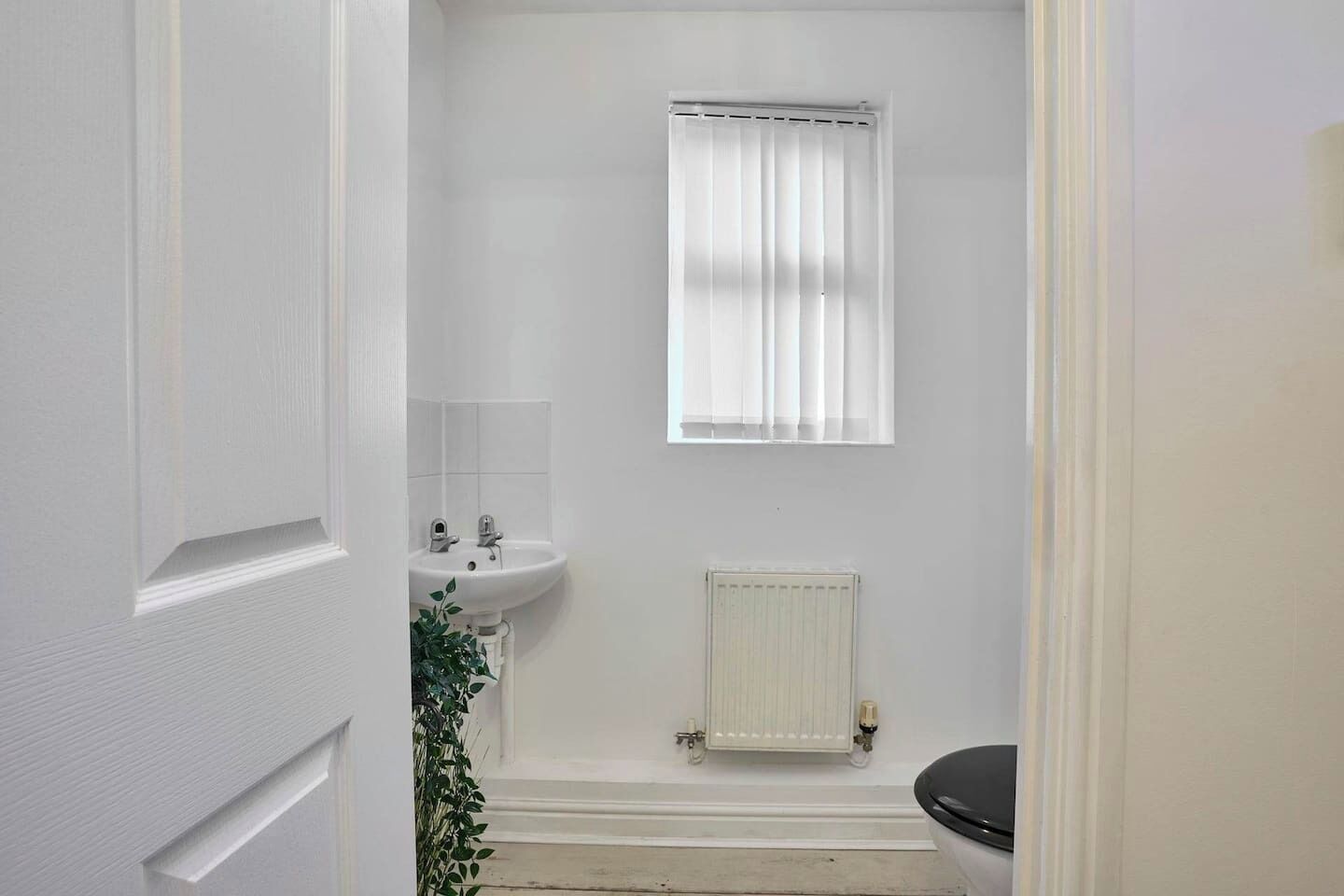 A bathroom with a white sink, a toilet, a window with curtains, and a radiator.