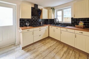 Eine Küche mit weißen Schränken, einer schwarzen Fliesenrückwand und einer Holzausziehtafel.