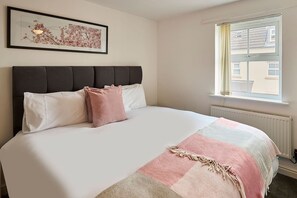 Ein Schlafzimmer mit einem Bett, einem Kopfteil, einem Fenster und einem gerahmten Bild an der Wand.