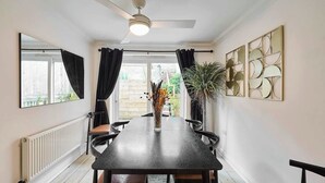 Uma sala de jantar com uma mesa comprida, cadeiras, um ventilador de teto e um vaso de planta.