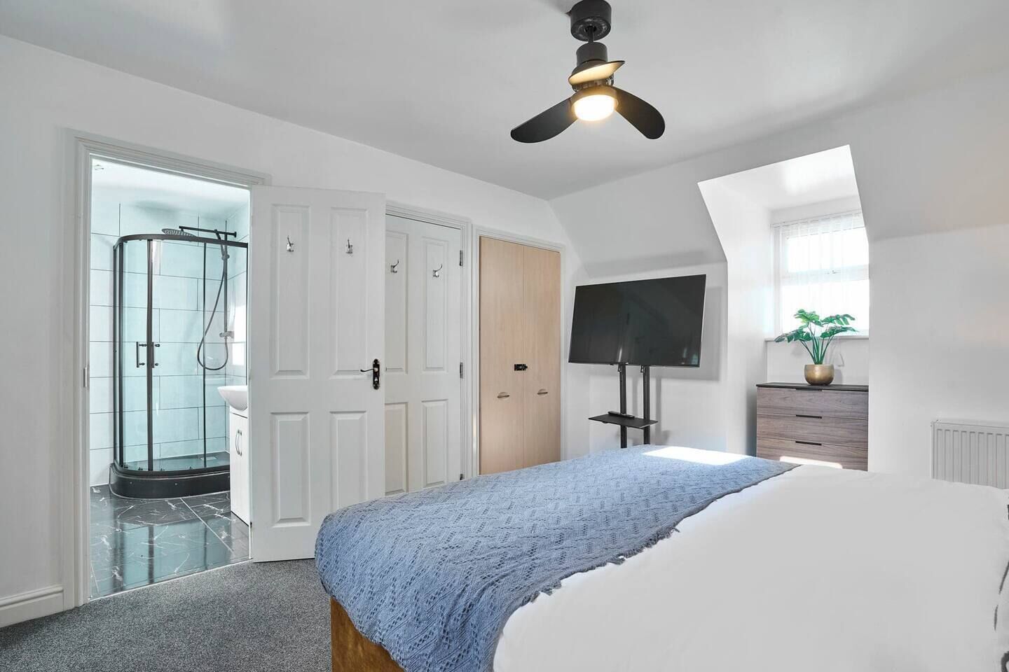 A bedroom with a bed, a TV mounted on the wall, a ceiling fan, and a shower area.
