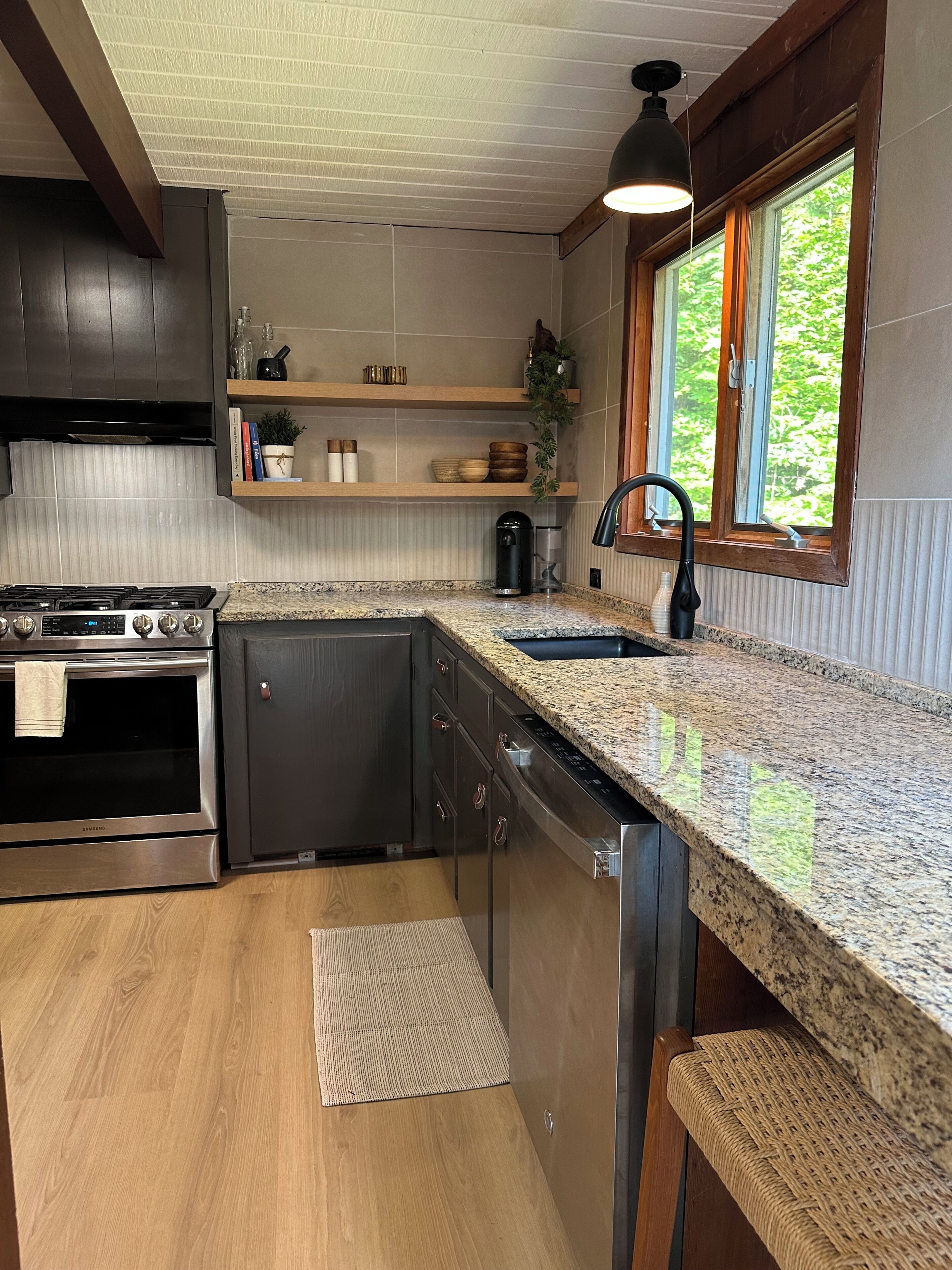 A modern kitchen with a stainless steel stove, granite countertop, and a window with a view of greenery.