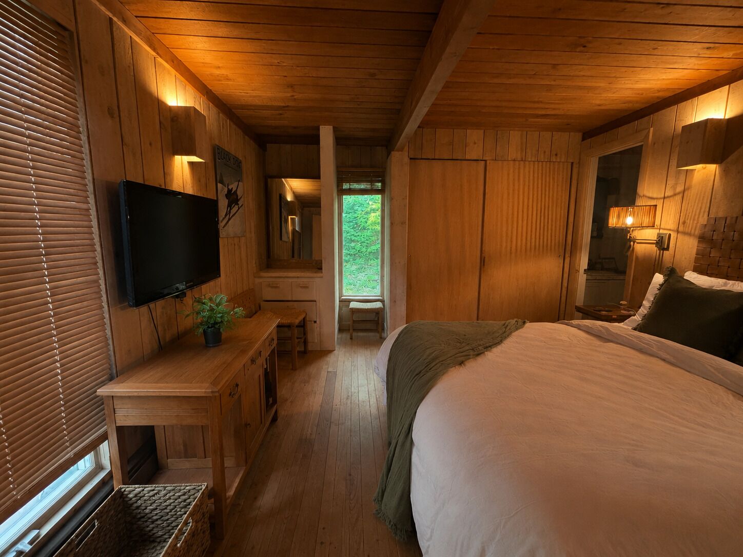 A wooden interior with a bed, a TV, a desk, and a window.